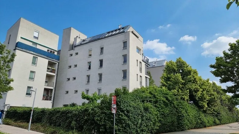 Moderne Wohngebäude mit weißer Fassade, Balkonen und üppiger grüner Bepflanzung unter blauem Himmel.