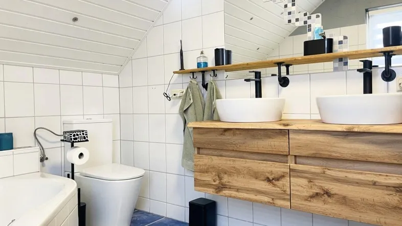 Modernes Badezimmer im Dachgeschoss mit zwei Aufsatzwaschbecken, Badewanne und blauen Fliesen.