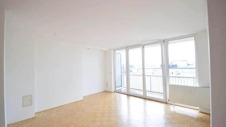 Helles Wohnzimmer mit Parkettboden, großen Fenstern und Zugang zu einem Balkon.