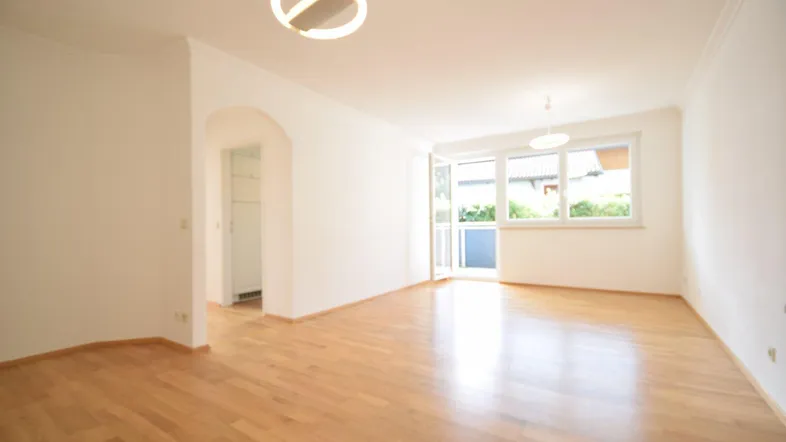 Helles Wohnzimmer mit Parkettboden, Zugang zum Balkon und weiß gestrichenen Wänden.