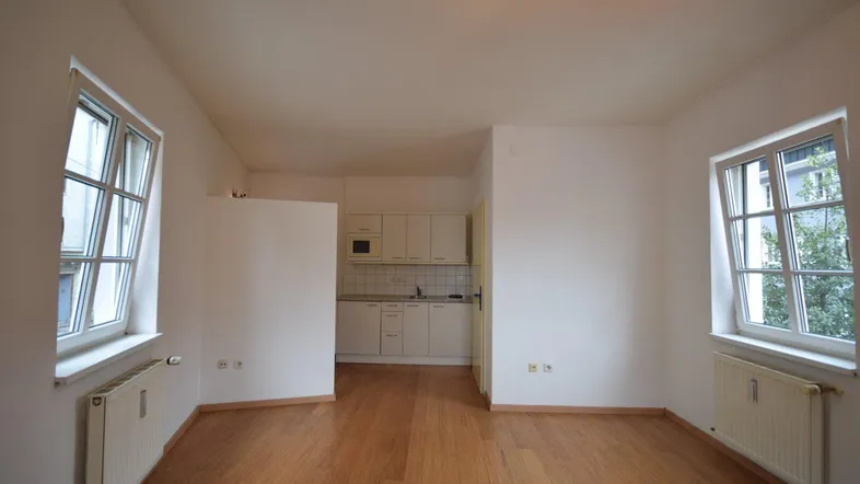 Heller Wohnbereich mit Holzfußboden und integrierter Küchenzeile, ideal für ein Studio-Apartment.