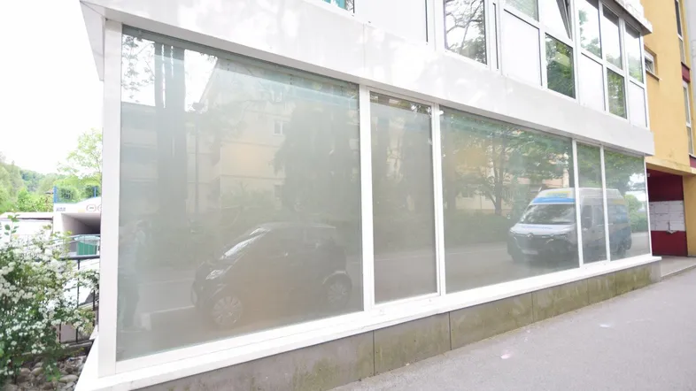 Ansicht der Gebäudefassade mit großen, undurchsichtigen Fenstern im Erdgeschoss und parkenden Autos davor.
