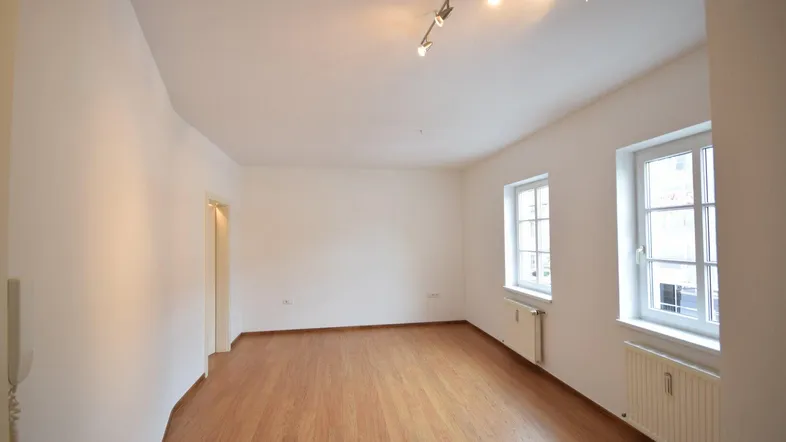 Helles Zimmer mit Holzboden und zwei Fenstern, bereit zur individuellen Gestaltung.
