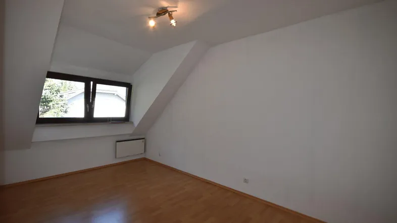 Helles Zimmer im Dachgeschoss mit Laminatboden, Fenster und schrägen Wänden.