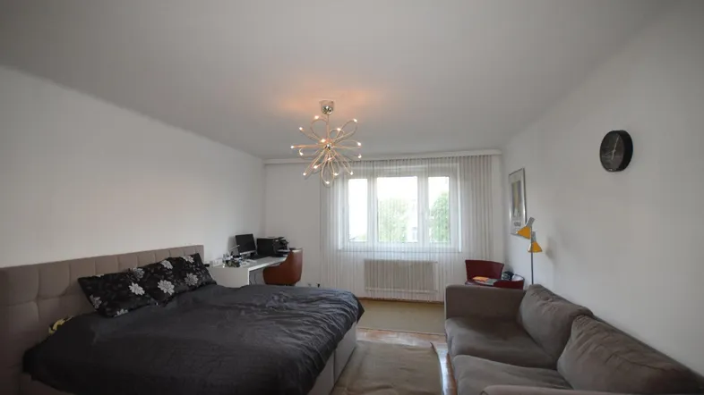 Helles Schlafzimmer mit großem Bett, Sofa und Arbeitsbereich am Fenster.