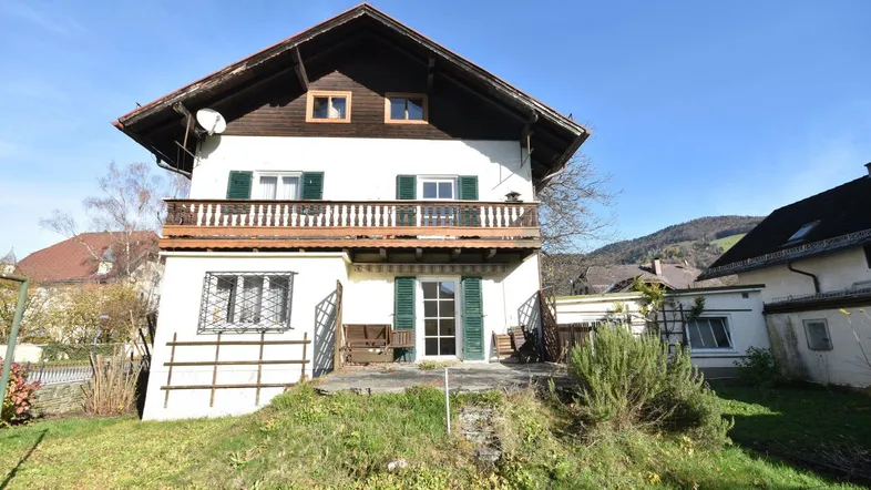 Traditionelles Haus mit Balkon und Gartenbereich in ländlicher Umgebung und Bergblick.