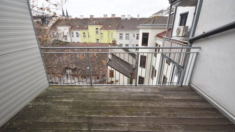 Kleiner Balkon mit Holzboden und Blick auf die umliegenden Dächer und Gebäude der Stadt.