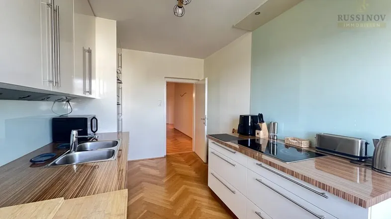 Moderne Küche mit weißen Hochglanzfronten, Holz-Arbeitsplatten und Parkettboden.