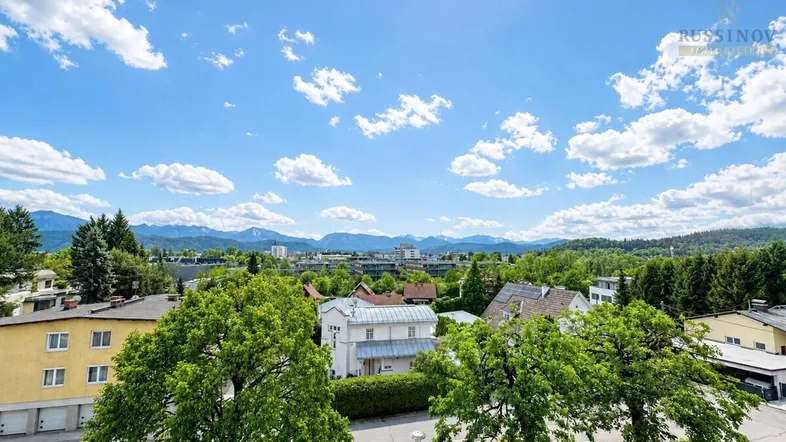 Weitläufiger Blick über die Stadt und die umliegende Berglandschaft unter blauem Himmel.