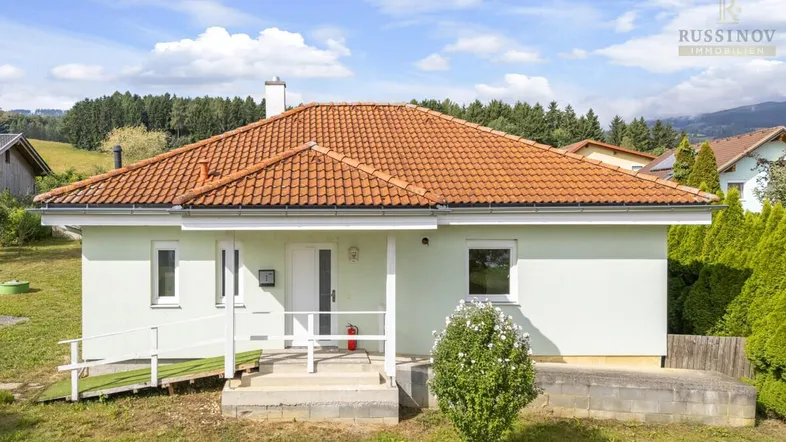 Einfamilienhaus mit hellgrüner Fassade, rotem Ziegeldach und einer kleinen Rampe am Eingangsbereich.
