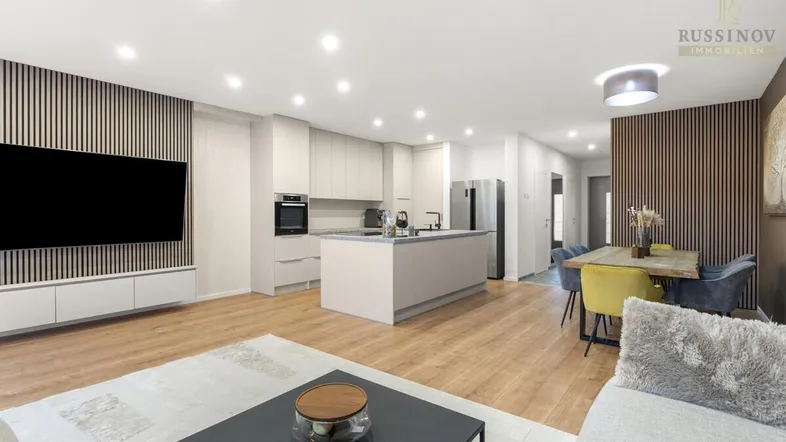 Moderner offener Wohn-Essbereich mit integrierter Küche, Holzboden und stilvoller Wandverkleidung.