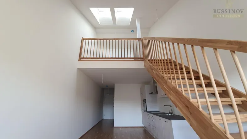 Heller offener Wohnbereich mit kleiner Küchenzeile, Holztreppe und Dachfenstern.