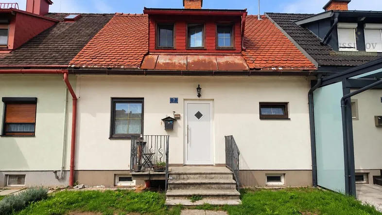 Frontansicht eines Reihenhauses mit rotem Ziegeldach und kleinen Fenstern.