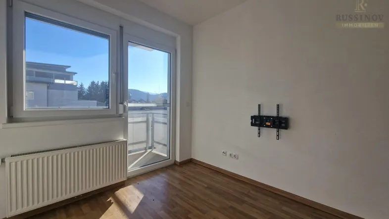 Helles Zimmer mit Holzboden und Zugang zu einem Balkon, ideal als Wohn- oder Schlafbereich.