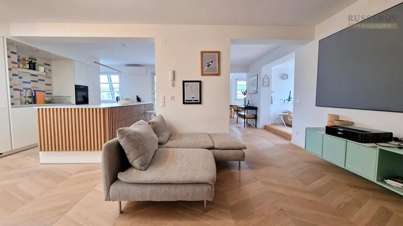 Helles, offenes Wohnzimmer mit Fischgrätparkett und integrierter Küche, ideal für modernes Wohnen.