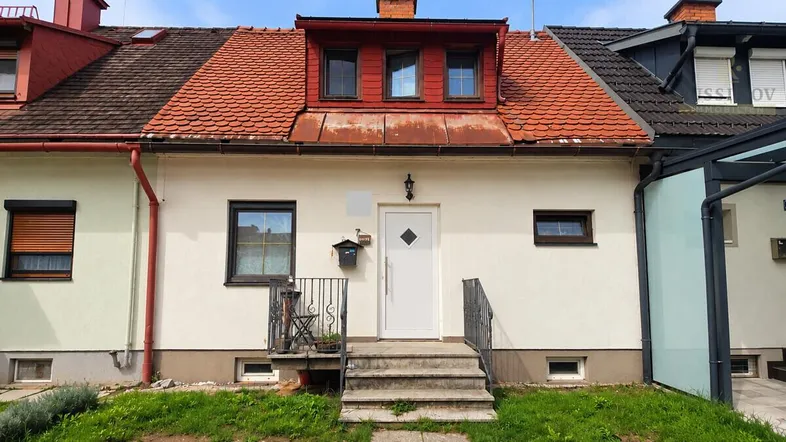 Frontansicht eines Reihenhauses mit rotem Ziegeldach, Dachgaube und kleinem Vorgarten.