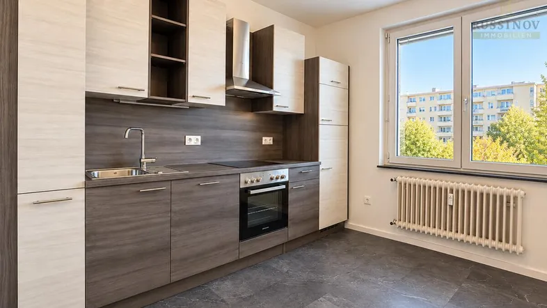 Moderne Einbauküche mit zweifarbigen Schränken, integrierten Geräten und Blick ins Grüne.