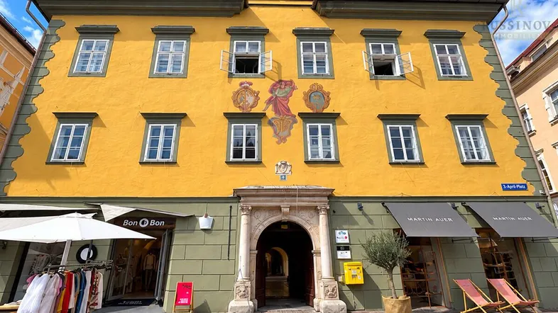 Historisches Gebäude mit gelber Fassade, verzierten Fenstern und Geschäften im Erdgeschoss.