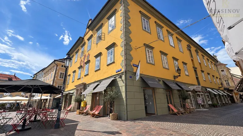 Historisches Gebäude mit gelber Fassade und Geschäften im Erdgeschoss an einem sonnigen Tag in der Stadt.