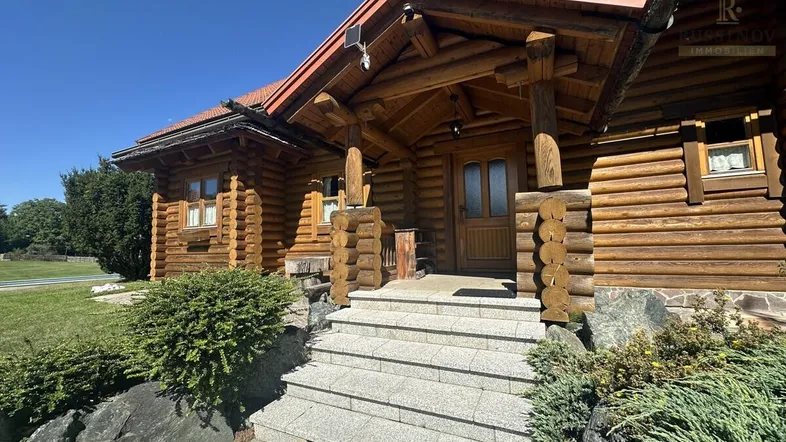 Traditionelles Holzhaus mit rustikalem Eingangsbereich und Steintreppe unter blauem Himmel.