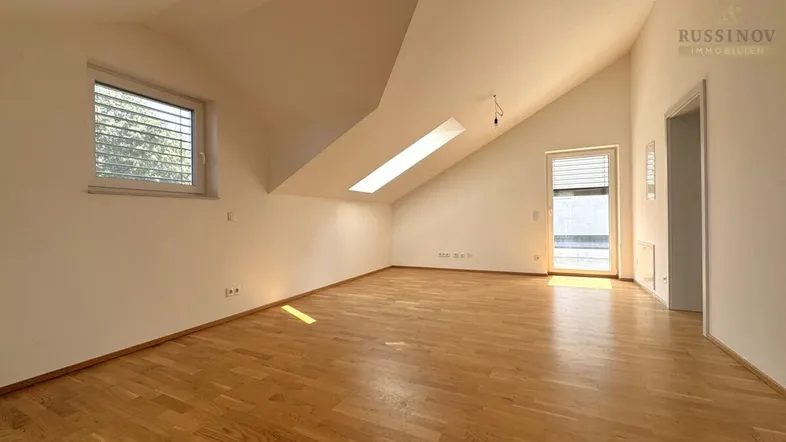 Helles Dachgeschosszimmer mit Holzboden, schrägen Wänden und Zugang zu einem Außenbereich.
