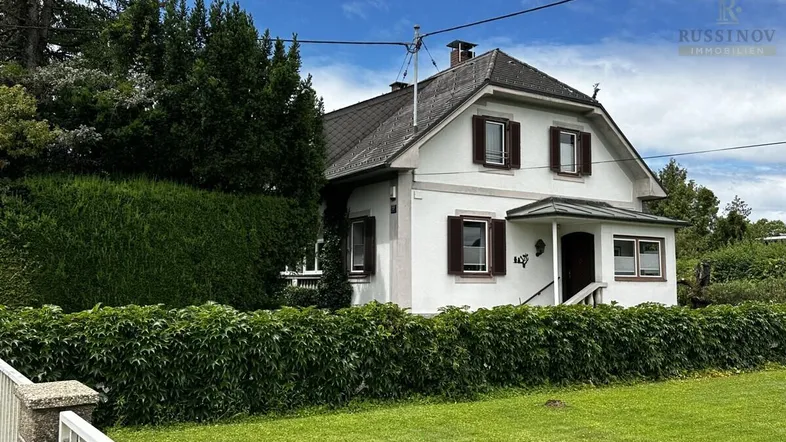 Charmantes Einfamilienhaus mit Satteldach, umgeben von gepflegtem Rasen und hohen Hecken.