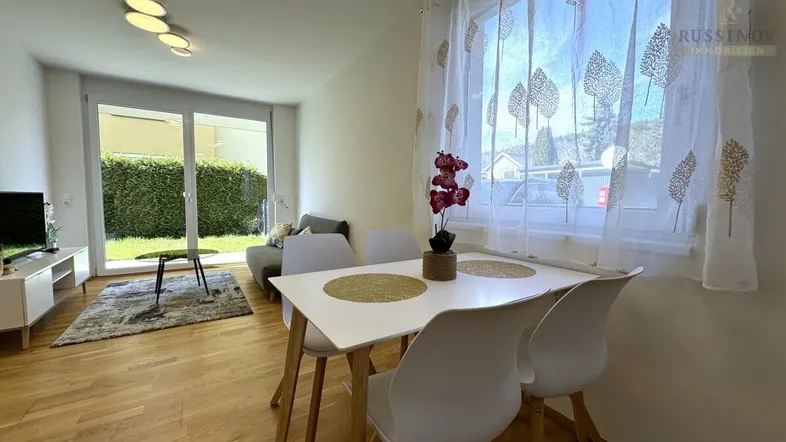 Helles Wohn- und Esszimmer mit Holzboden, Zugang zum Garten und moderner Einrichtung.