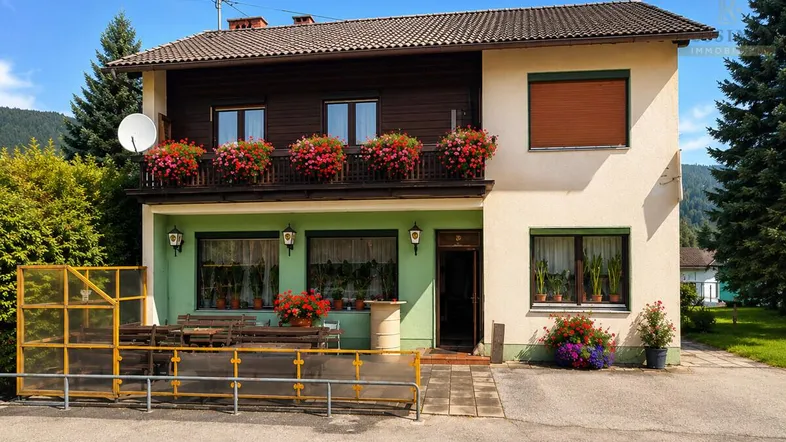 Traditionelles Haus mit Balkon, Blumenkästen und einem kleinen Außenbereich mit Tischen.