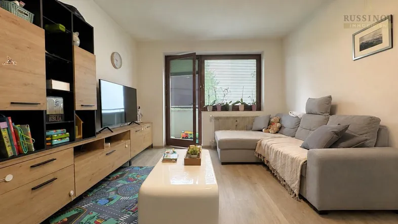 Helles Wohnzimmer mit gemütlichem Sofa, TV-Möbeln und Zugang zu einem Balkon.
