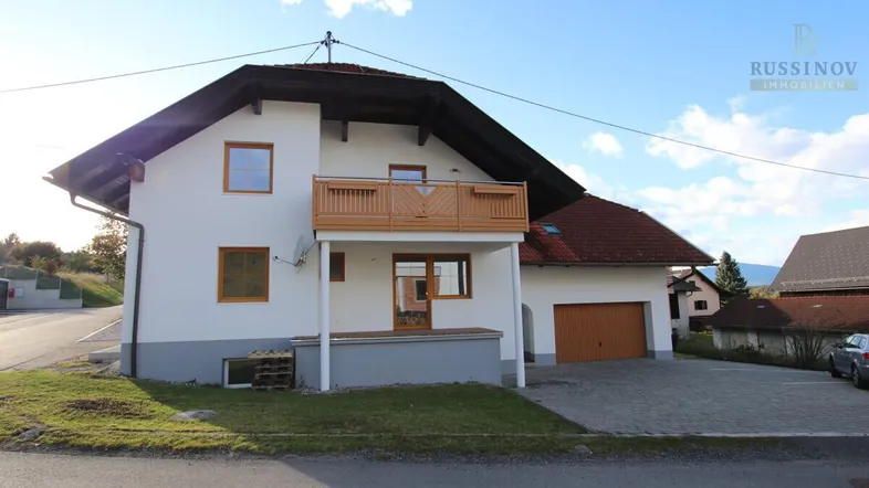 Das gepflegte Einfamilienhaus präsentiert sich mit einem Balkon und integrierter Garage in ländlicher Umgebung.