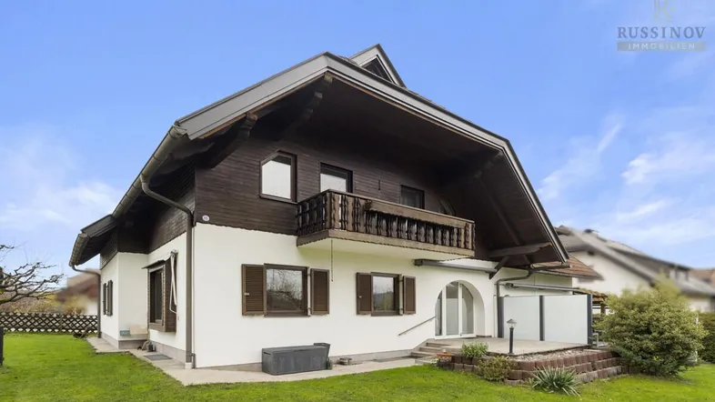 Charmantes Chalet mit weißer Fassade, Holzelementen und Balkon, umgeben von einem grünen Garten.