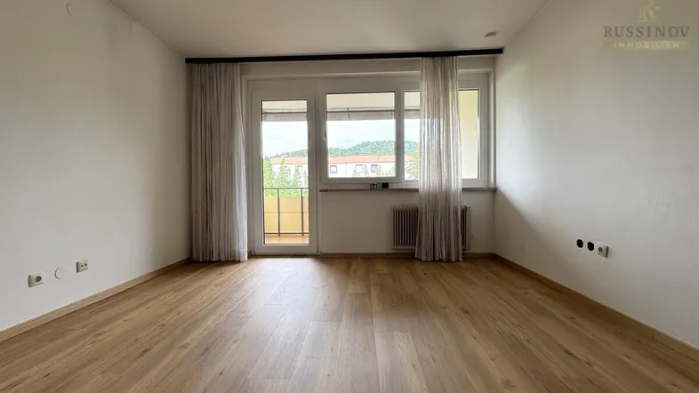 Helles Zimmer mit modernem Laminatboden, weißen Wänden und Zugang zu einem Balkon.