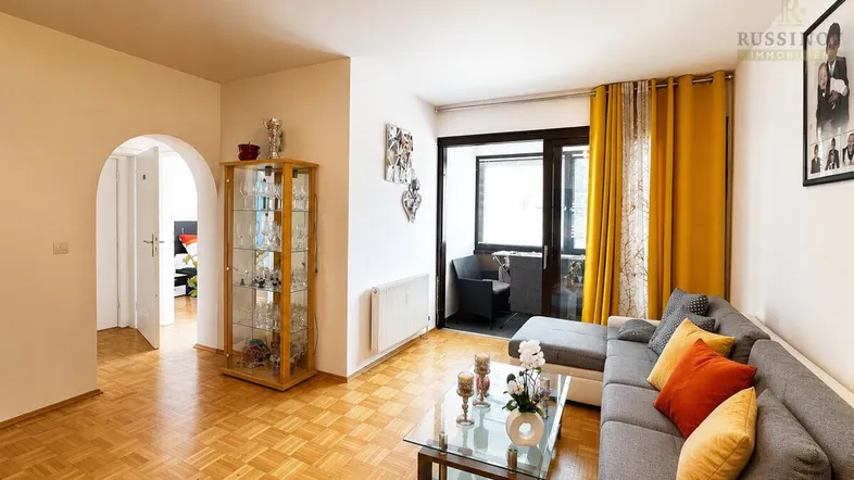 Helles Wohnzimmer mit Parkettboden, gemütlichem Sofa und Zugang zu einem kleinen Balkon.