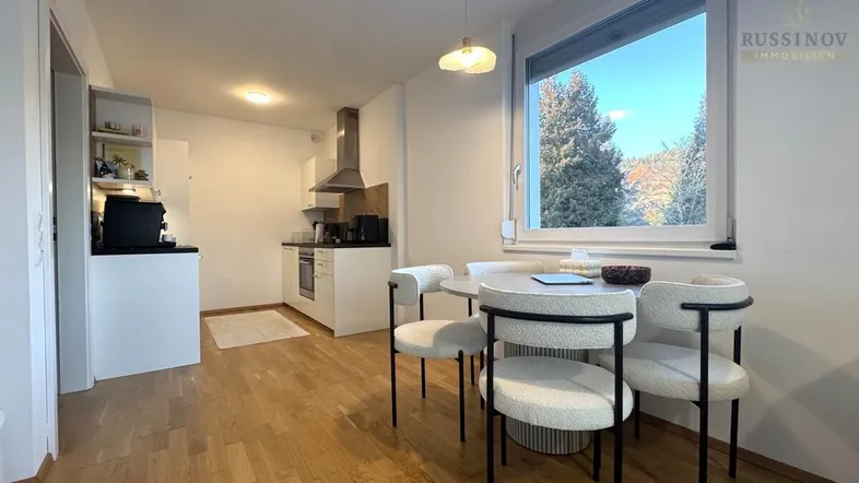 Heller offener Wohn-Essbereich mit integrierter Küche, Parkettboden und großem Fenster.