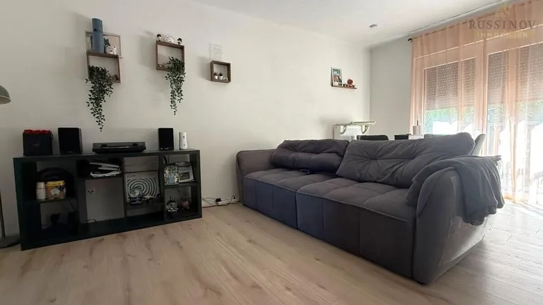 Helles Wohnzimmer mit modernem Sofa, Holzboden und Blick nach draußen durch große Fenster.