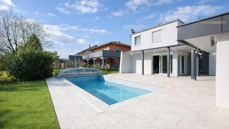 Moderner Außenbereich mit großem Pool, weitläufiger Terrasse und gepflegtem Rasen unter blauem Himmel.