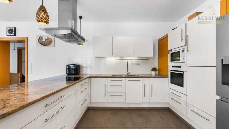 Moderne Küche mit weißen Schränken, Granitarbeitsplatte und integrierten Geräten, ideal für kulinarische Aktivitäten.