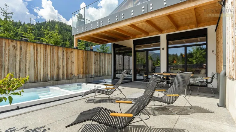 Geräumige Terrasse mit Whirlpool, Liegestühlen und Essbereich, umgeben von einer Holzwand und Bergblick.