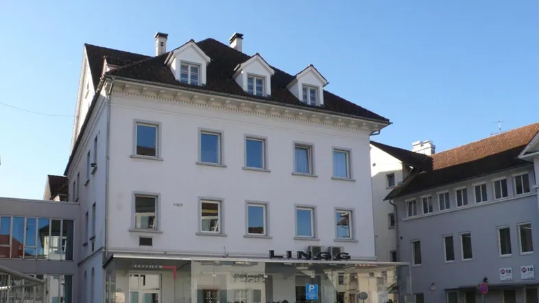 Traditionelles Geschäftsgebäude mit weißer Fassade, vielen Fenstern und einem Laden im Erdgeschoss unter blauem Himmel.