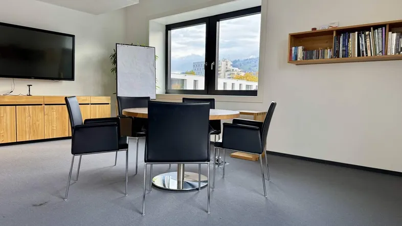 Moderner Konferenzraum mit rundem Tisch, schwarzen Stühlen und Blick auf die Berge durch große Fenster.