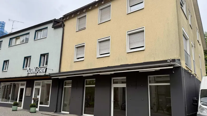 Gelbe Fassade eines Mehrfamilienhauses mit dunklem Erdgeschoss und großen Schaufenstern.