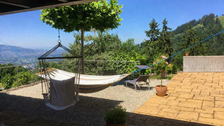 Geräumige Terrasse mit Hängematte, Liegestuhl und weitem Blick über die grüne Landschaft.