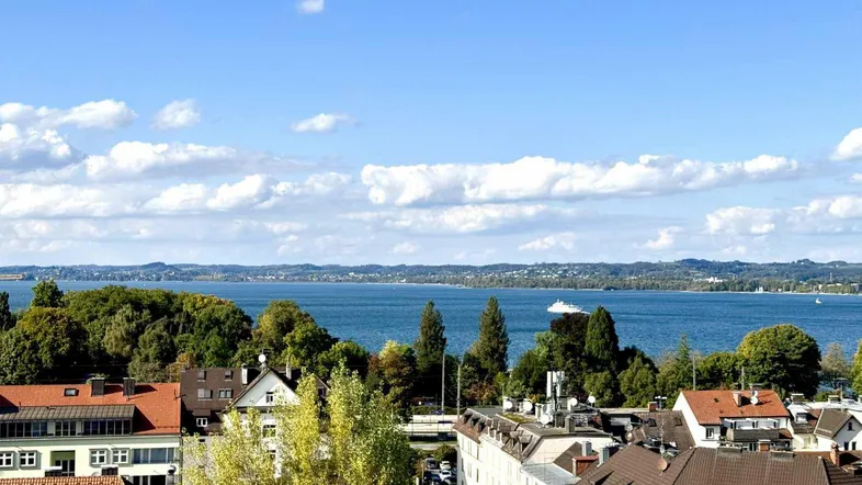 Panoramablick über die Stadt und den See mit bewaldeten Ufern unter blauem Himmel.