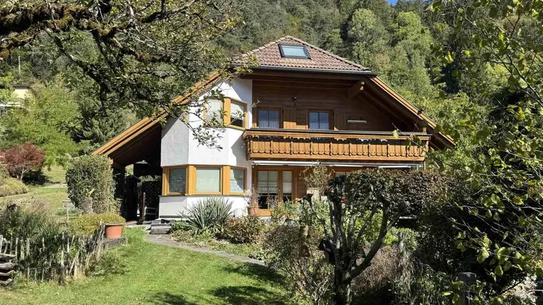 Charmantes Haus mit Holzbalkon und gepflegtem Garten in bergiger Umgebung.