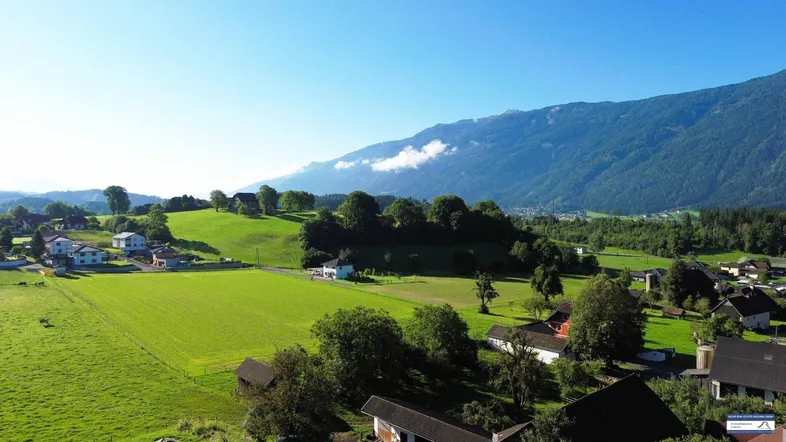 Weitläufige Luftaufnahme der ländlichen Umgebung mit grünen Feldern und Bergen im Hintergrund.