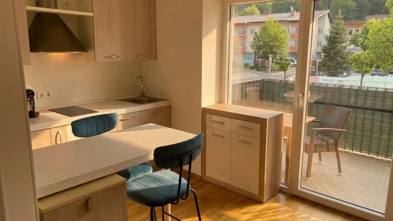 Helle Küche mit Holzelementen, integriertem Essbereich und Zugang zum Balkon.