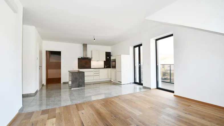 Helles, offenes Wohnzimmer mit integrierter Küche, Parkettboden und Zugang zum Balkon.