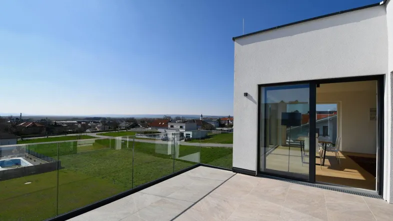 Geräumige Dachterrasse mit Glasgeländer und weitem Blick über die Landschaft und umliegende Häuser.