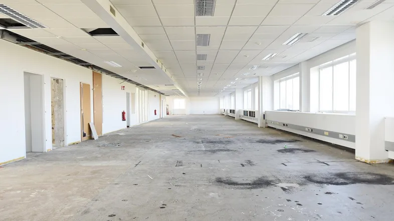 Großer, leerer Büroraum mit Betonboden und vielen Fenstern, bereit für den Ausbau.