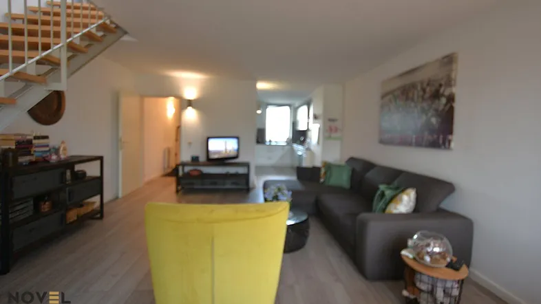 Helles Wohnzimmer mit modernem Sofa, gelbem Sessel und offener Treppe zum Obergeschoss.